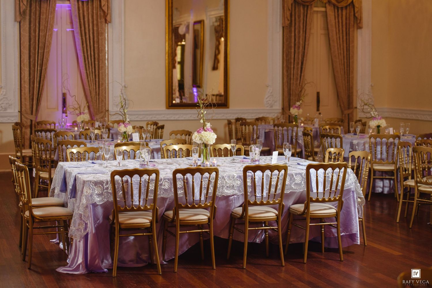 Elegant wedding reception hall with gold Chiavari chairs, lavender-draped tables, and ornate decor in a grand ballroom.