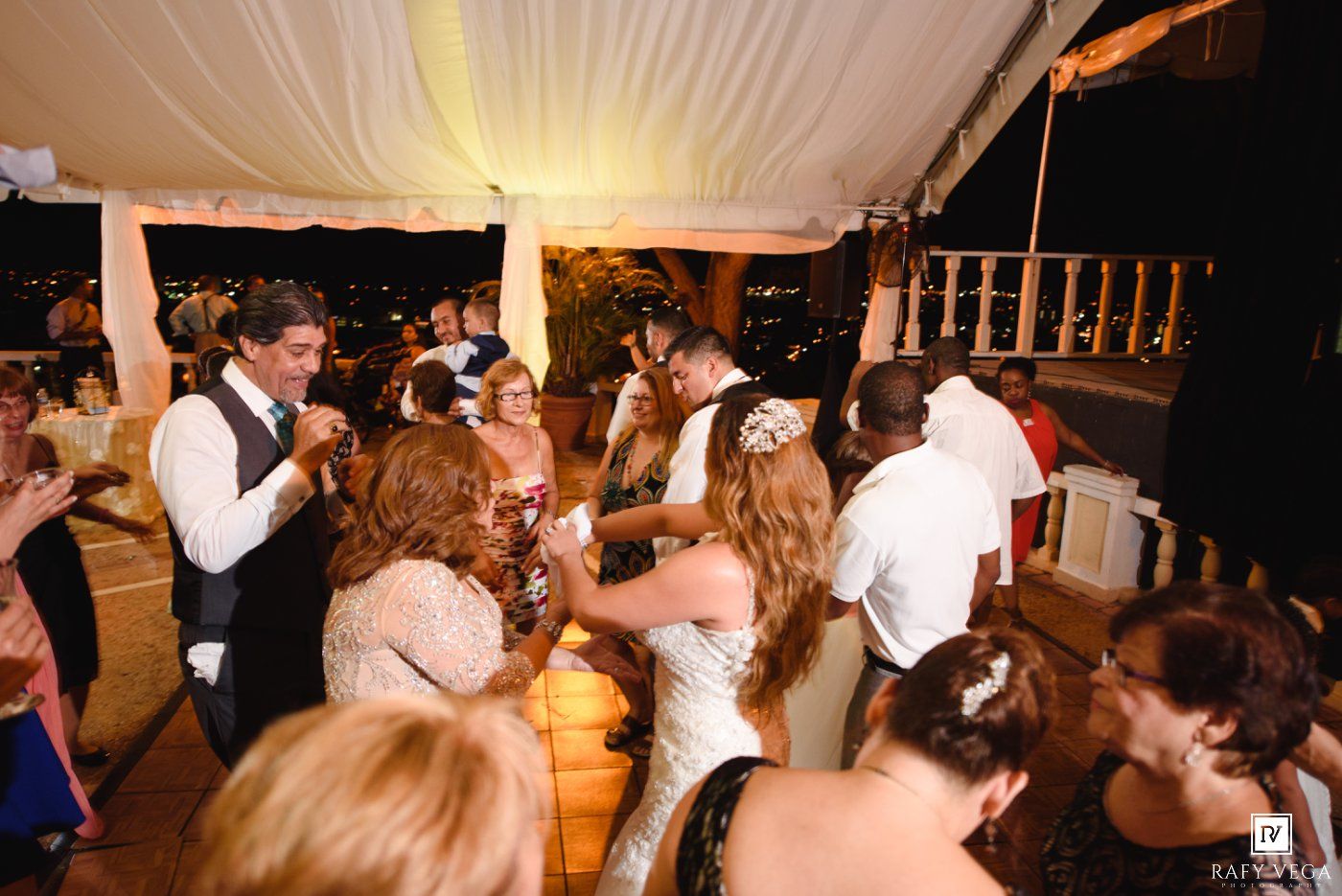 Guests dancing and celebrating at an elegant outdoor wedding reception under a white tent at night.