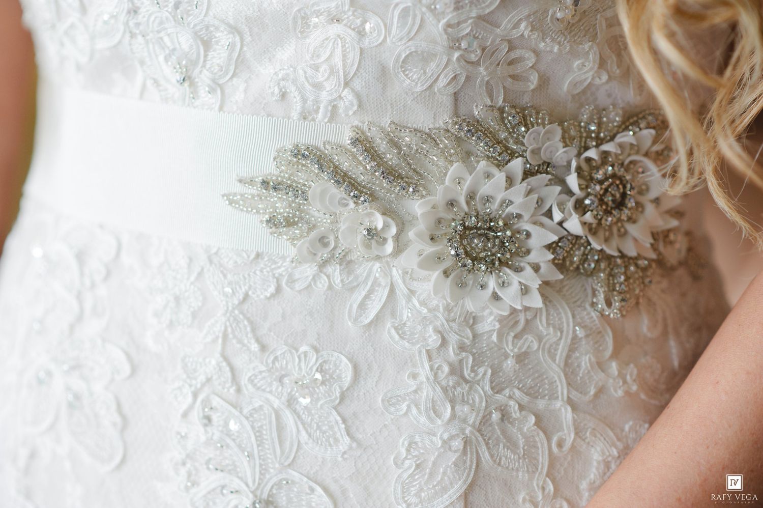 Close-up of a bridal gown with intricate lace detailing and a rhinestone floral sash belt.