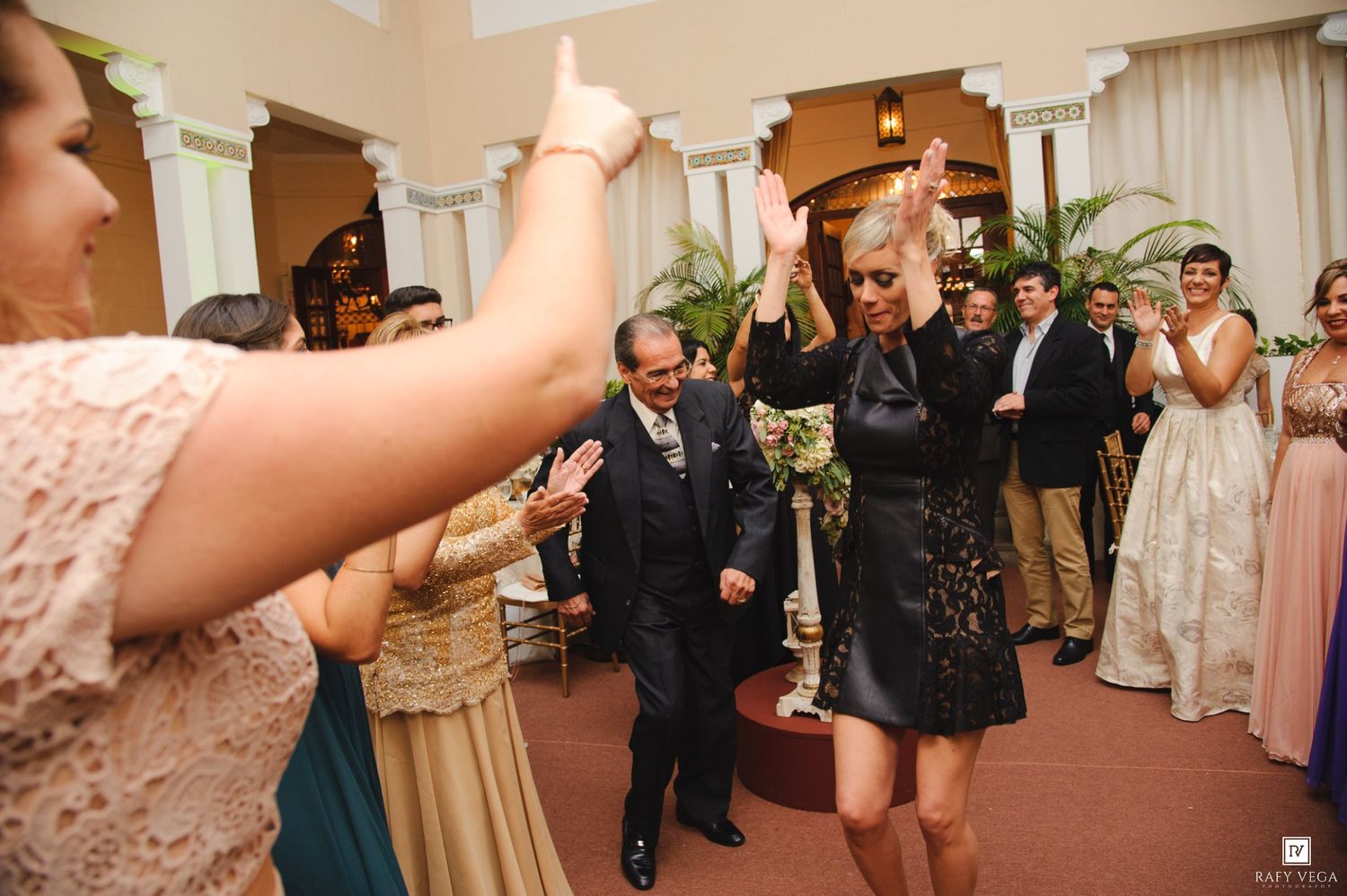 Guests celebrate at a wedding reception as a couple walks through a cheering crowd in an elegant venue.