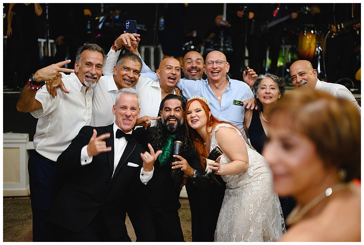 Joyful wedding reception group photo with bride, groom, and guests celebrating on the dance floor.