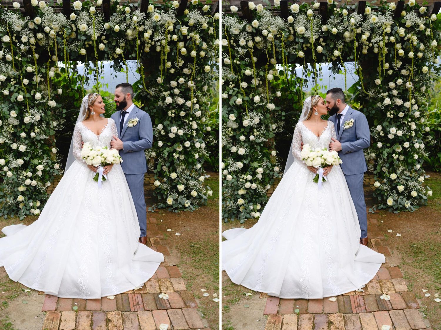 Bride and groom pose under a lush floral arch with white blooms and greenery on their wedding day.