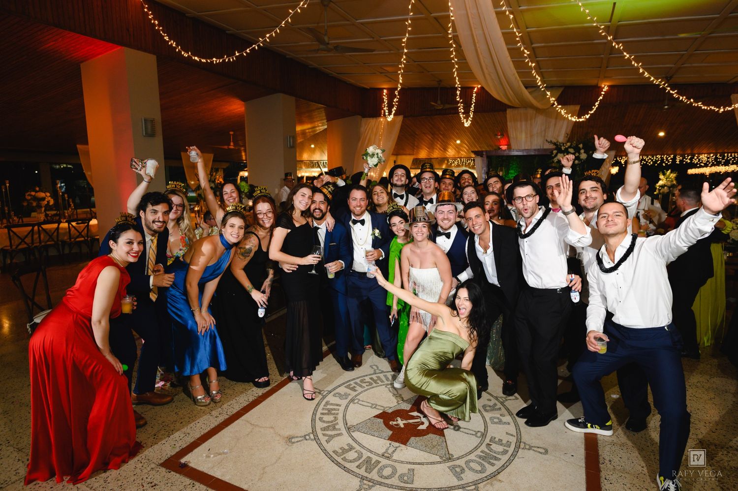 Large group of elegantly dressed wedding guests celebrating together on a decorated dance floor at a reception.