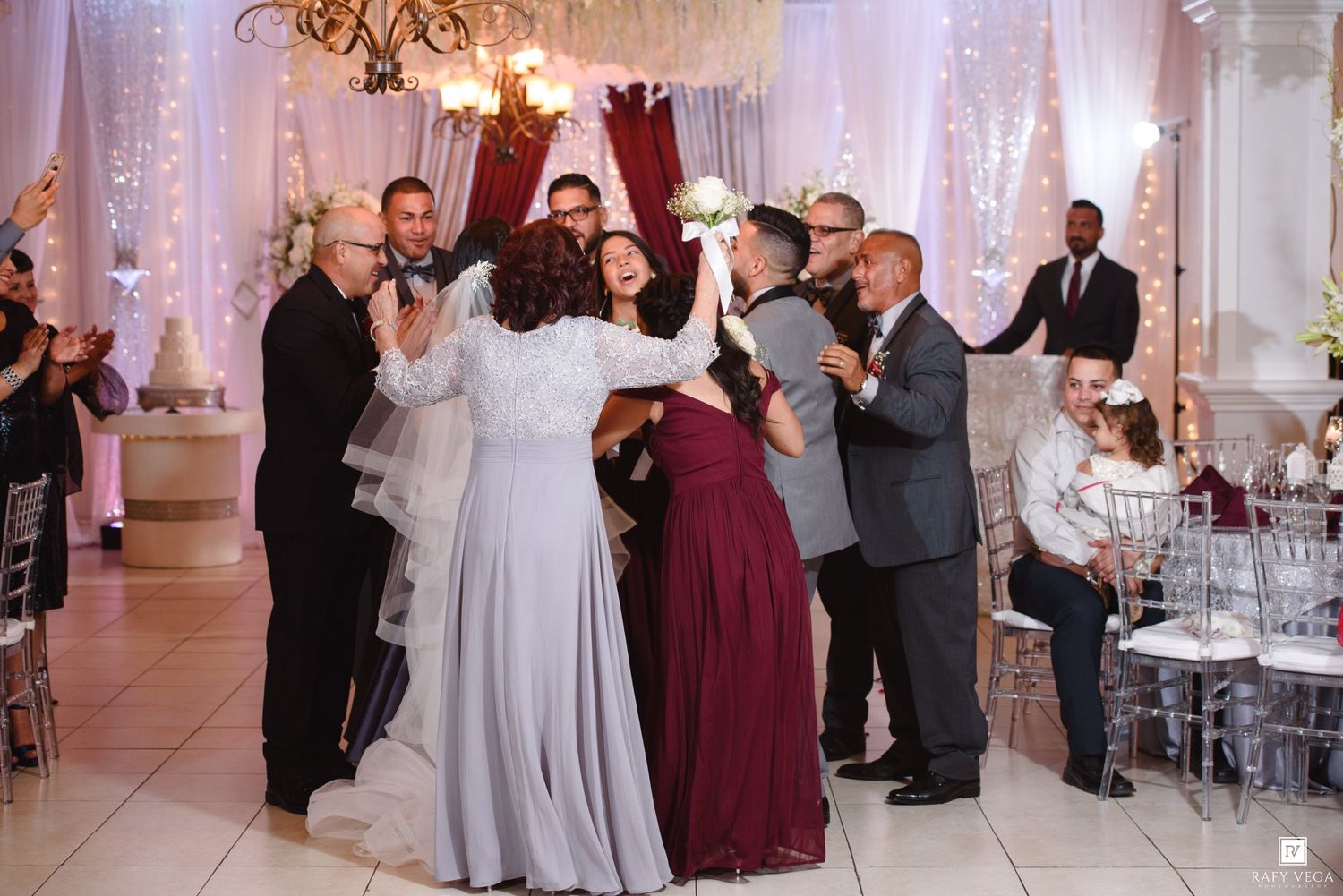 Wedding guests celebrate on the dance floor at an elegant reception venue with fairy lights and draped decor.