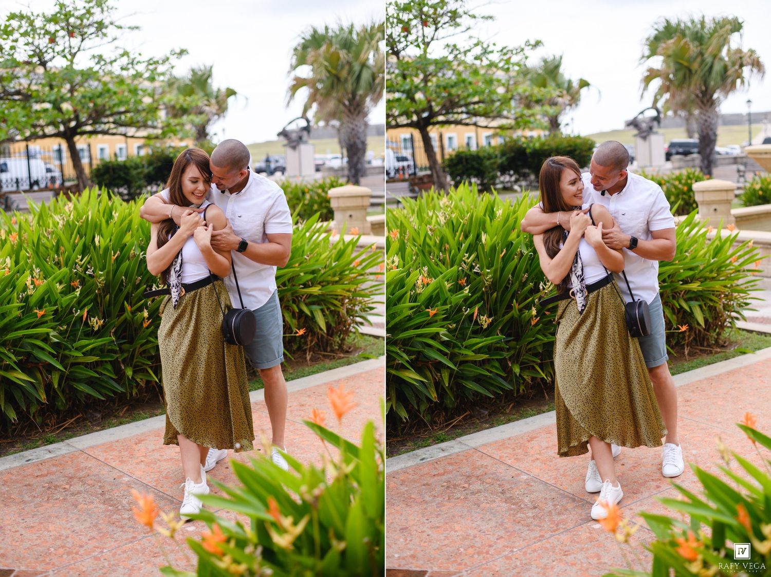 Couple embracing and laughing together outdoors near tropical greenery, woman in olive skirt and man in white shirt.