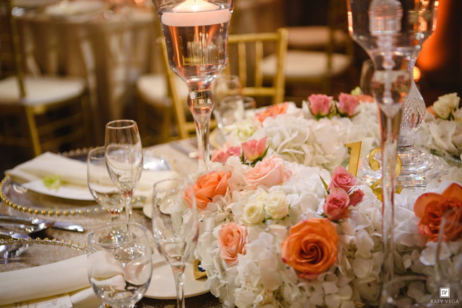 Elegant wedding reception table with orange and white floral centerpiece, crystal candelabras, and gold charger plates.