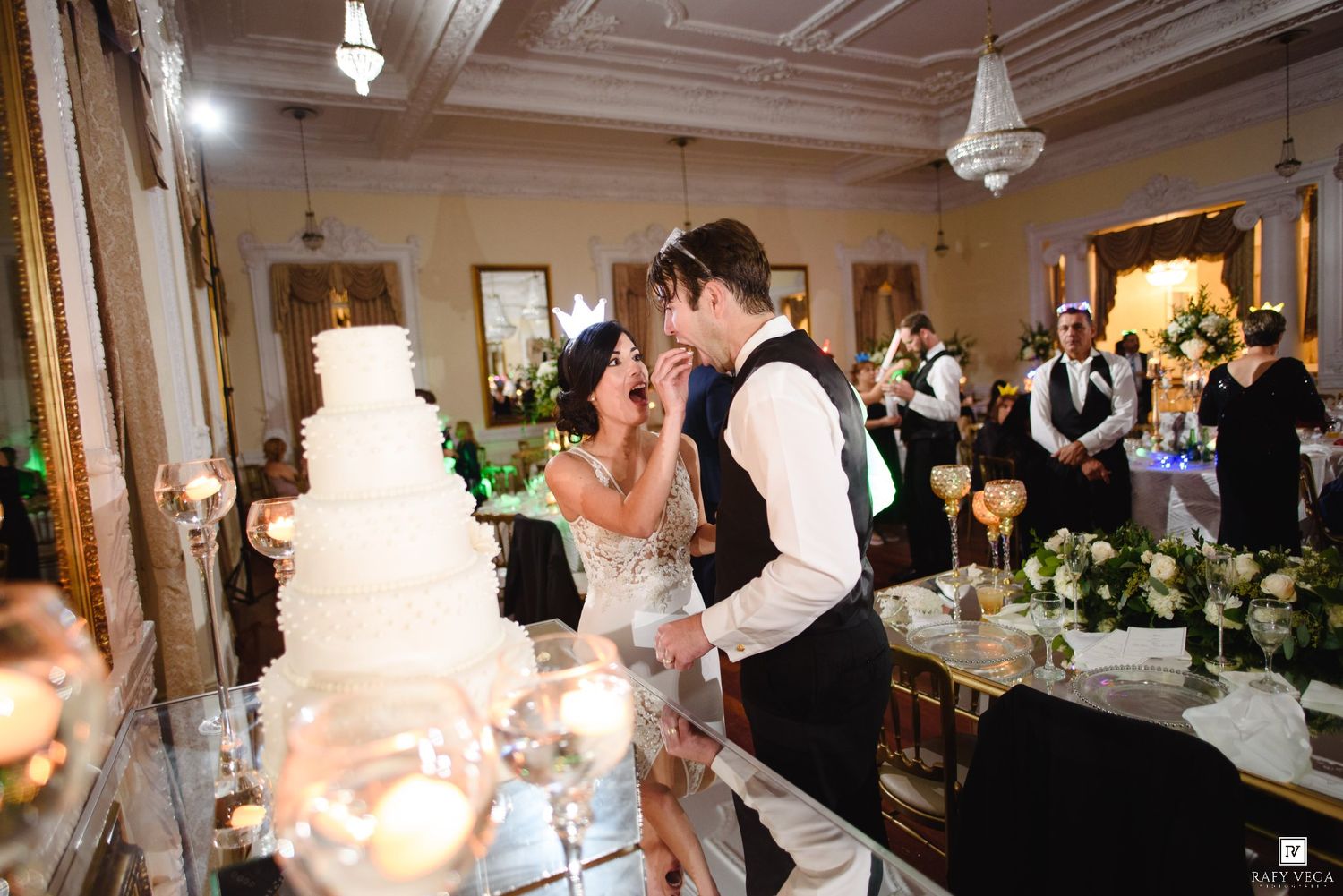 Bride and groom share a kiss while cutting their elegant white wedding cake at a romantic reception venue.