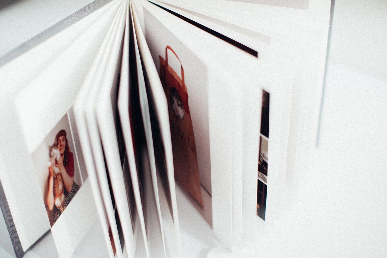 Open photo album with colorful printed photographs on thick white pages, displayed on a light surface.