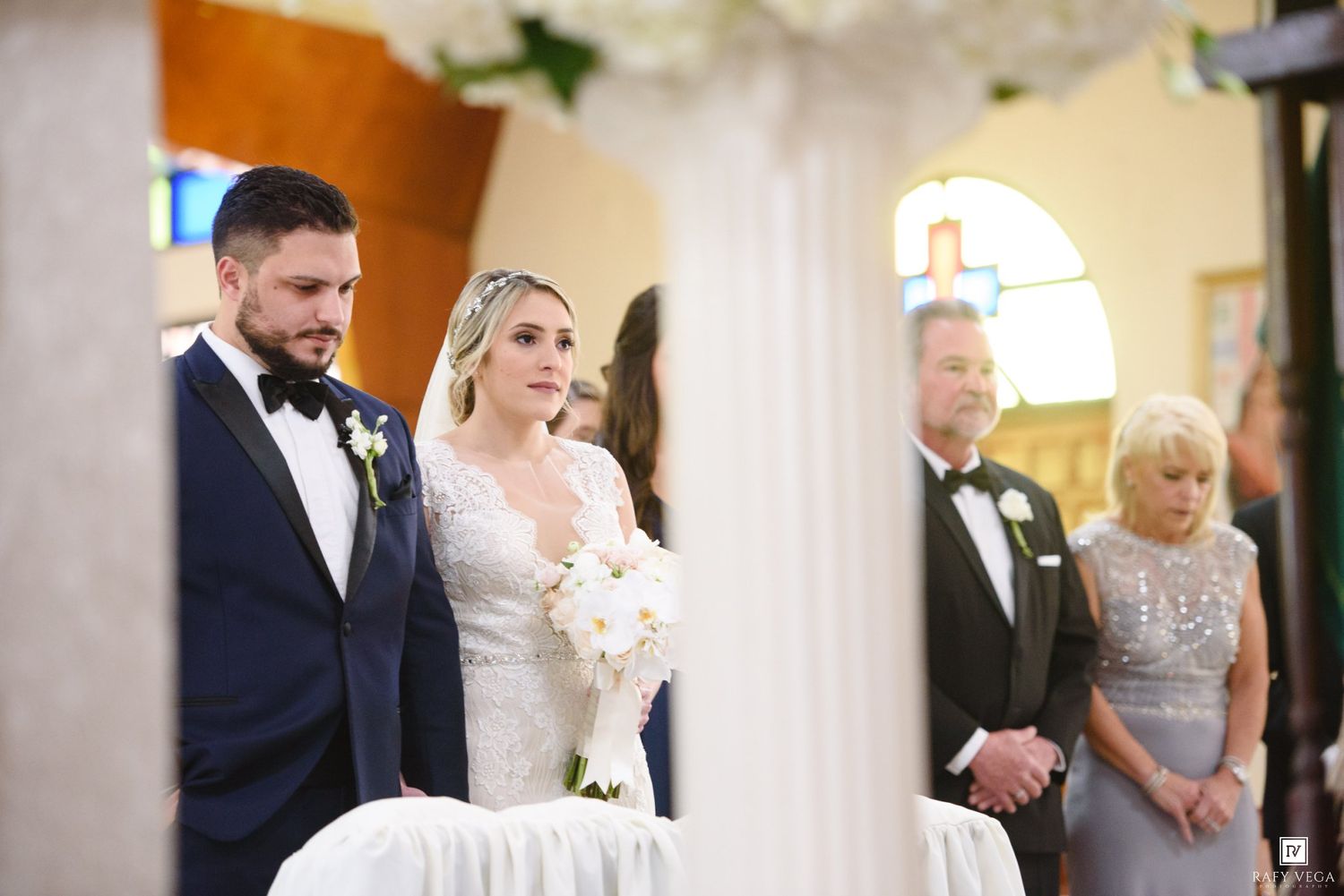Bride and groom stand at the altar during a church wedding ceremony, bride holding white floral bouquet.