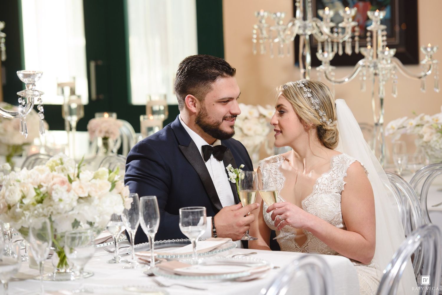 Bride and groom share a romantic moment at their elegant wedding reception table adorned with white floral centerpieces.
