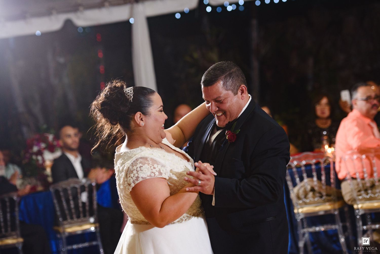 Bride and groom share emotional first dance moment at romantic outdoor wedding reception with gold chairs.