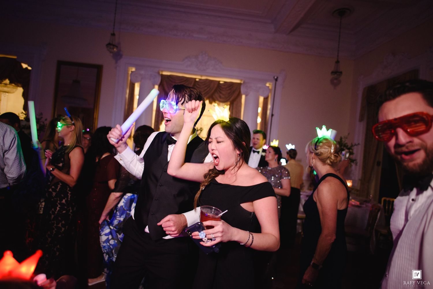 Wedding guests dance and celebrate wearing colorful masks and glow accessories at lively reception party.