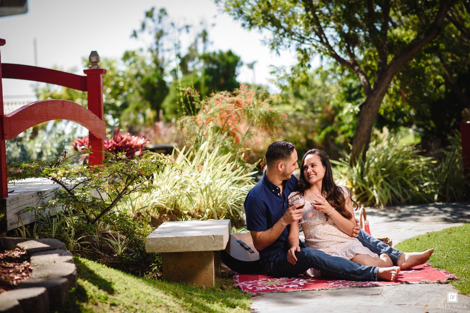 Couple sharing wine on a picnic blanket in a lush garden park, enjoying a romantic outdoor engagement session.