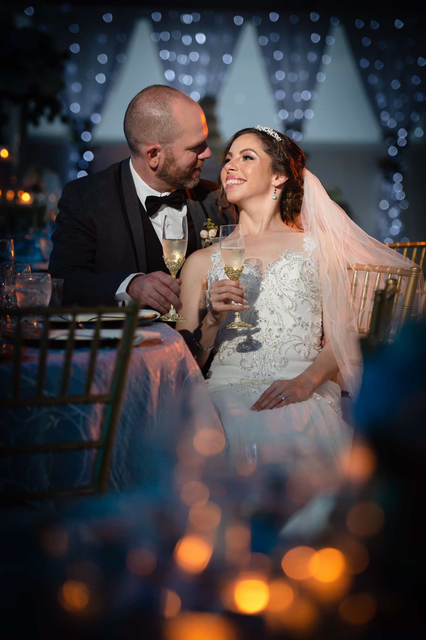 Bride and groom share a romantic toast with champagne at their elegant wedding reception with bokeh lights.