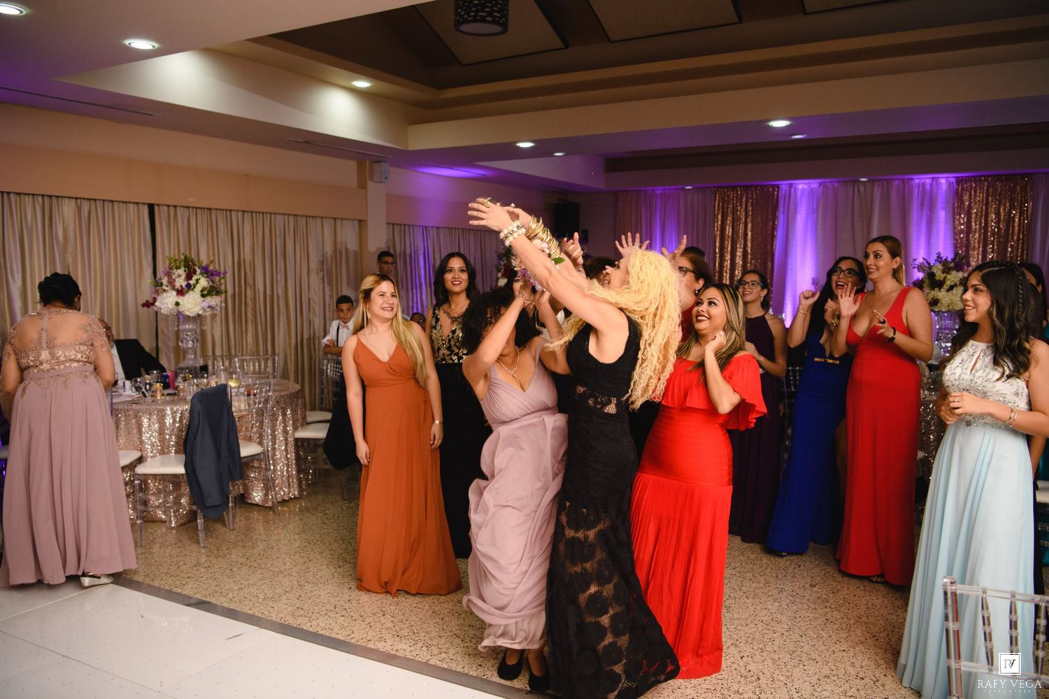 Wedding guests in formal gowns celebrating on dance floor at elegant reception venue.