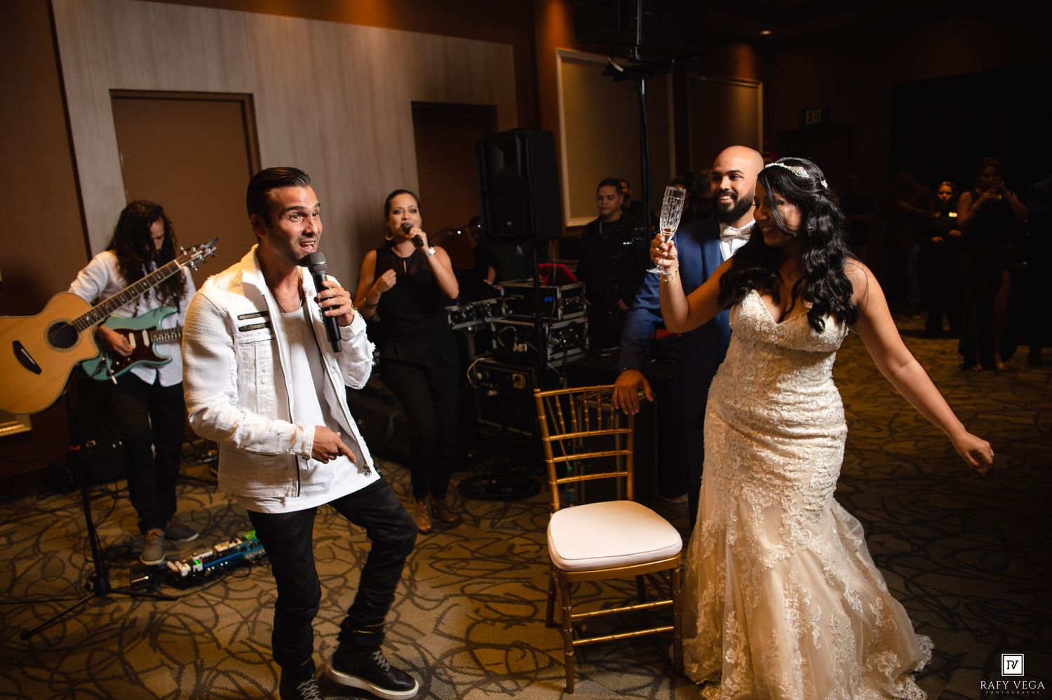 Singer performing with microphone at wedding reception as bride and groom dance in elegant ballroom venue.