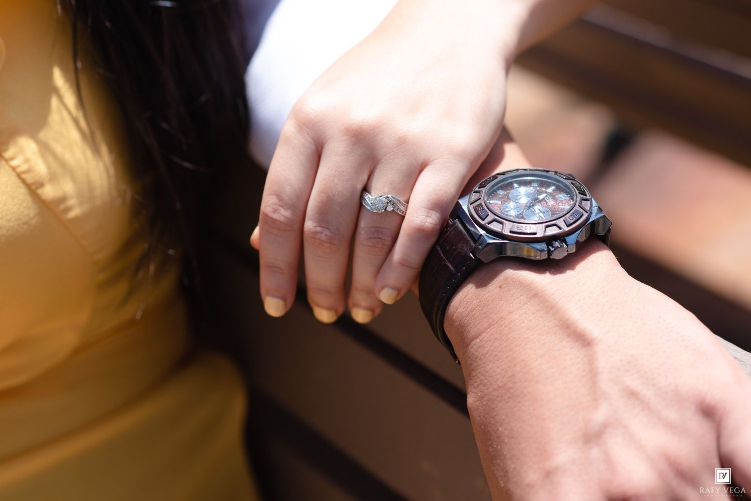 Close-up of a woman's hand with a diamond ring resting on a man's wrist wearing a large sport watch.