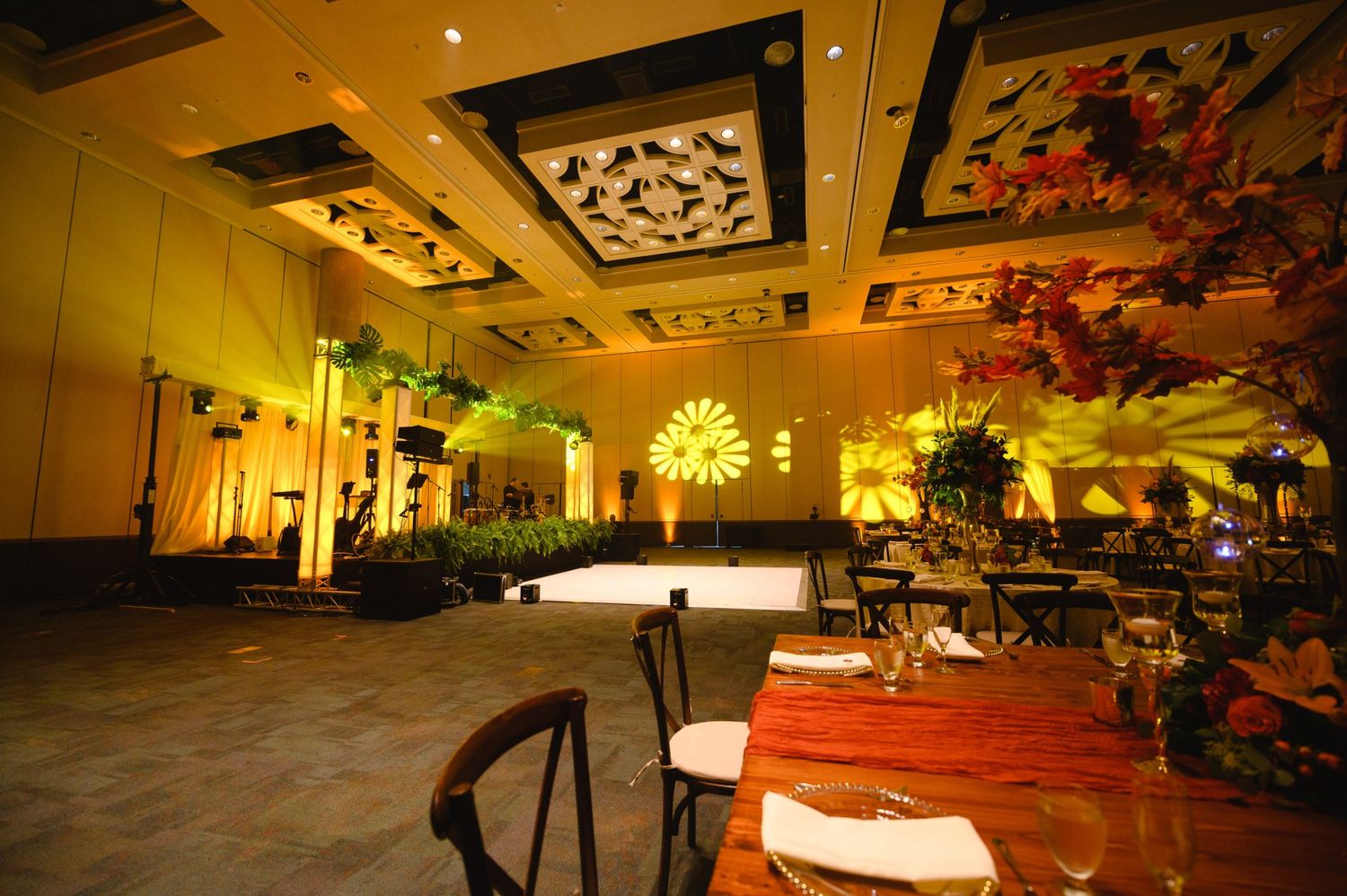 Elegant ballroom event venue with warm golden lighting, decorated tables, floral arrangements, and a dance floor.