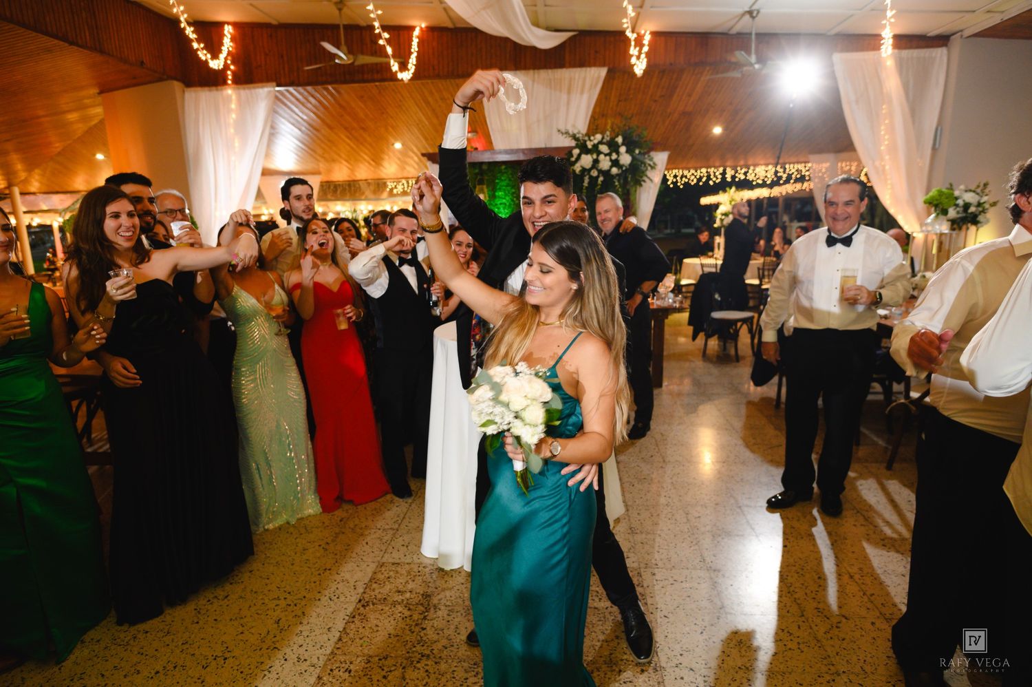 Couple dancing at elegant wedding reception with guests in formal attire on decorated dance floor.