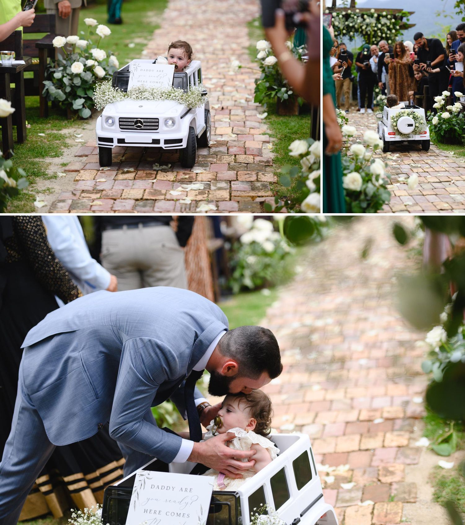 Child rides toy Mercedes down wedding aisle decorated with white flowers as guests watch the ceremony.