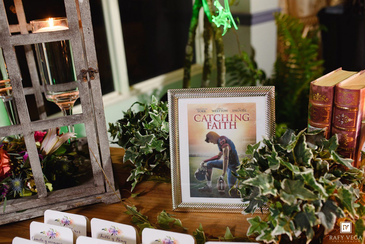 Framed Catching Faith movie poster displayed on a decorated table with ivy, books, and candles at an elegant event.