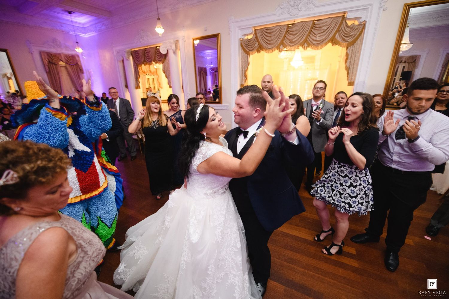 Bride and groom share joyful first dance surrounded by cheering guests in elegant ballroom wedding reception.