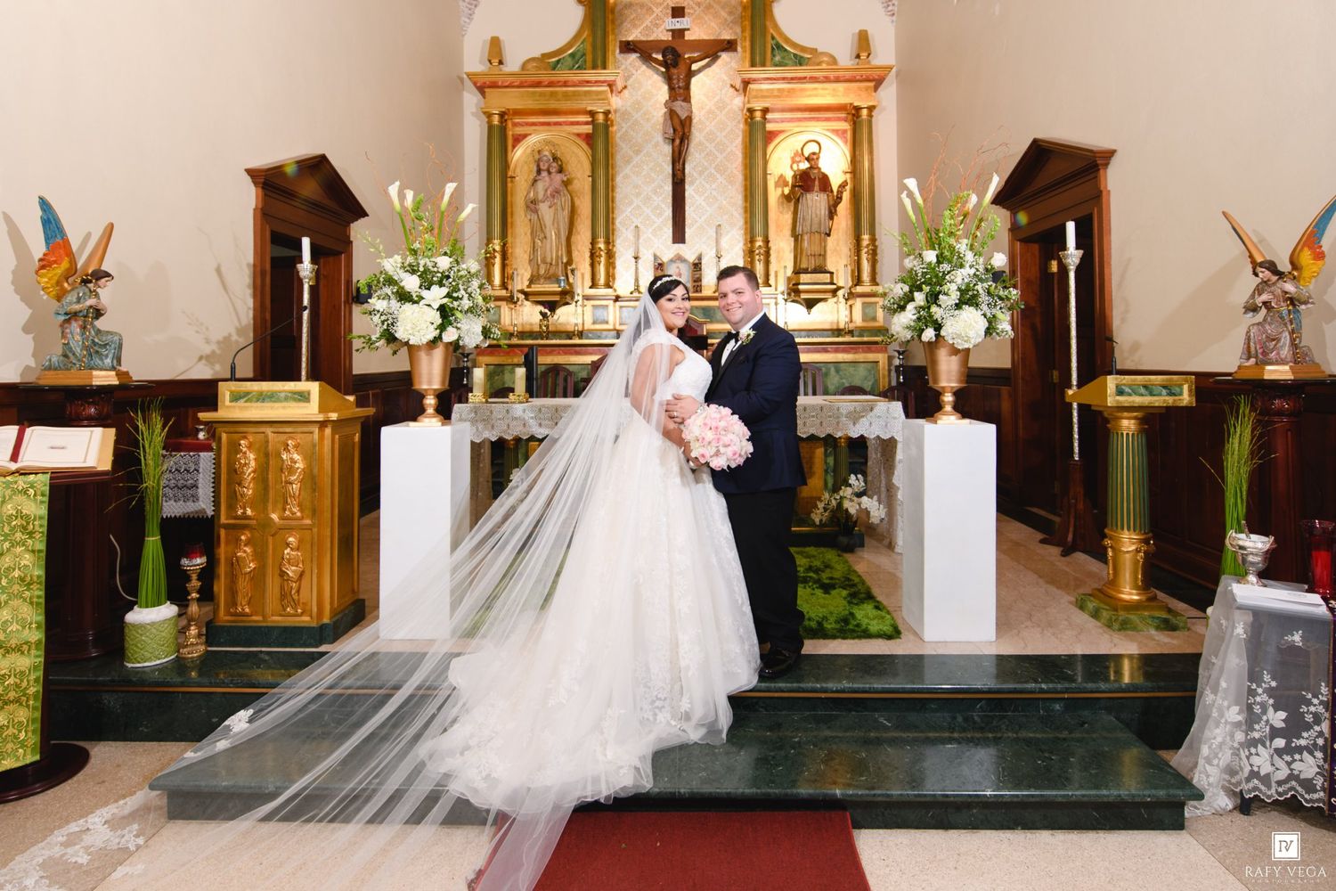 Bride and groom share a romantic moment at the church altar during their wedding ceremony, surrounded by floral arrangements.