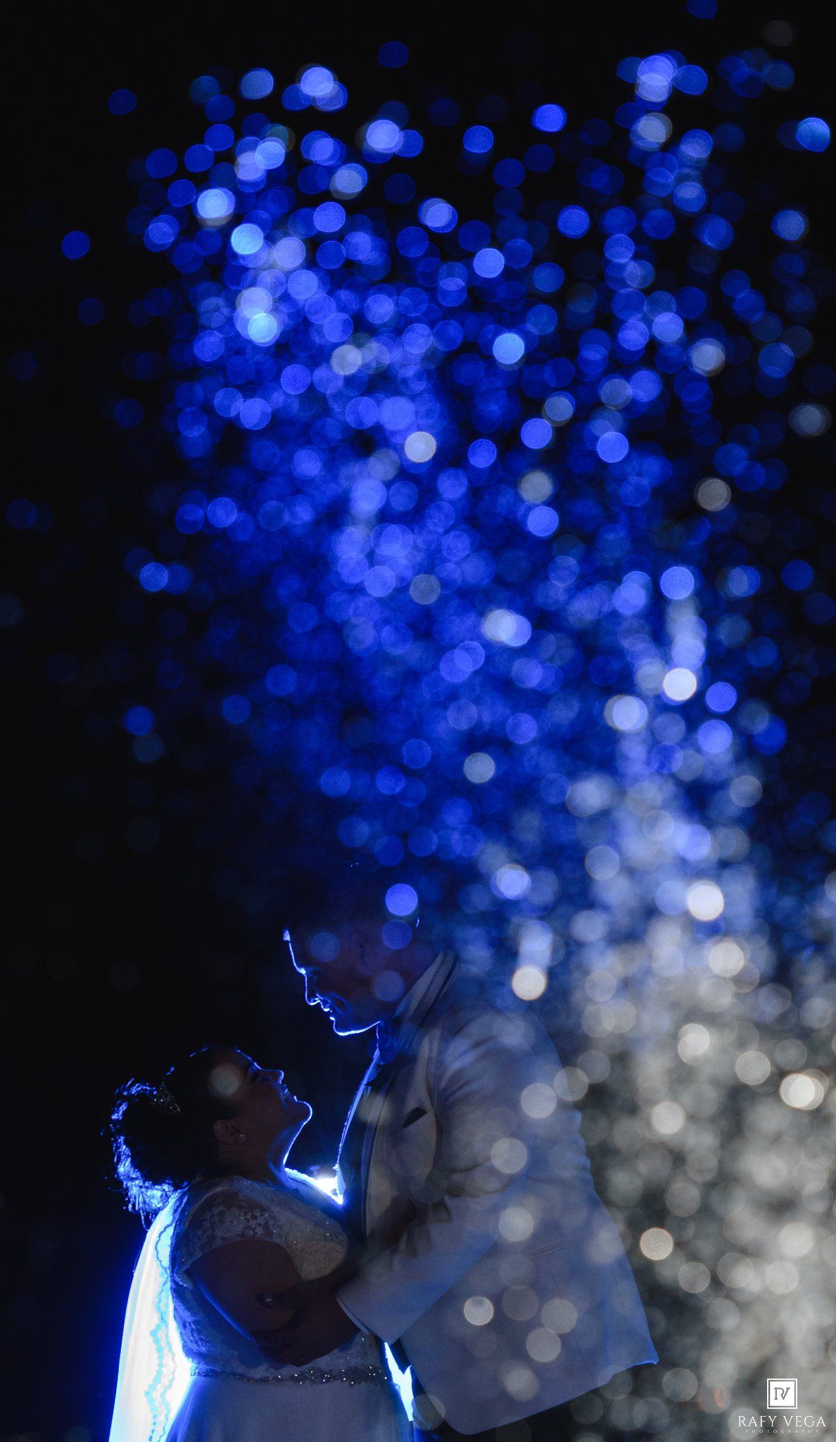 Bride and groom share romantic first dance surrounded by stunning blue bokeh lights at elegant wedding reception.