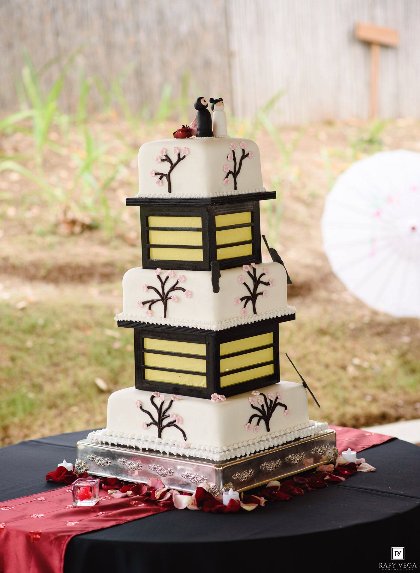 Four-tier Japanese pagoda-inspired wedding cake with cherry blossom branches and lantern design on black tablecloth.