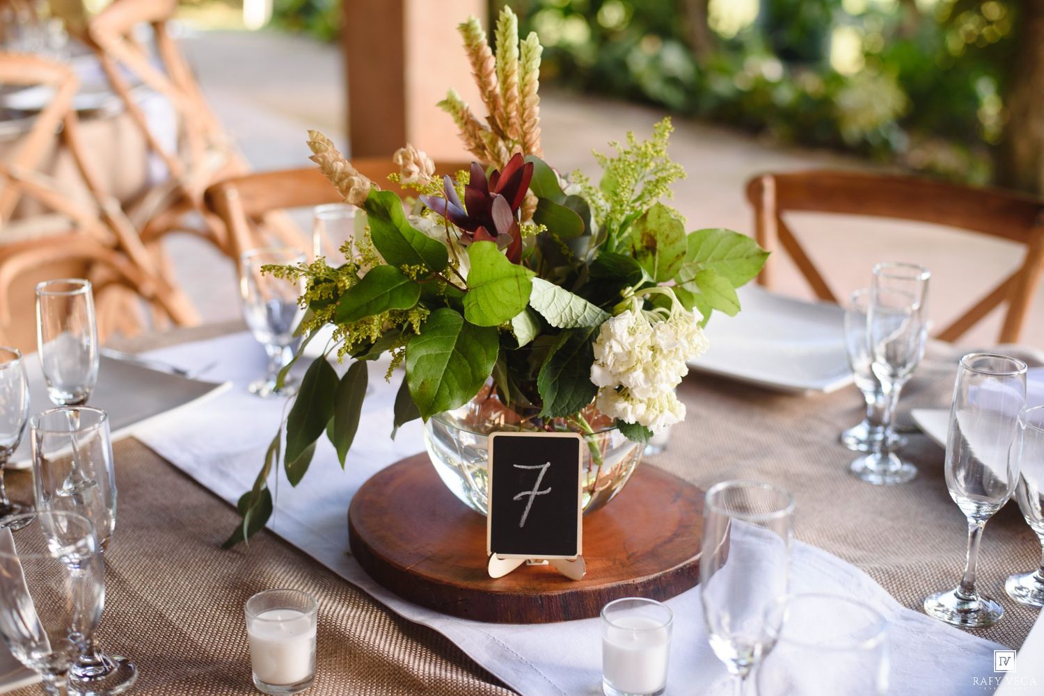 Elegant wedding table centerpiece with lush greenery, floral arrangement, and a chalkboard table number 7 on a wooden base.