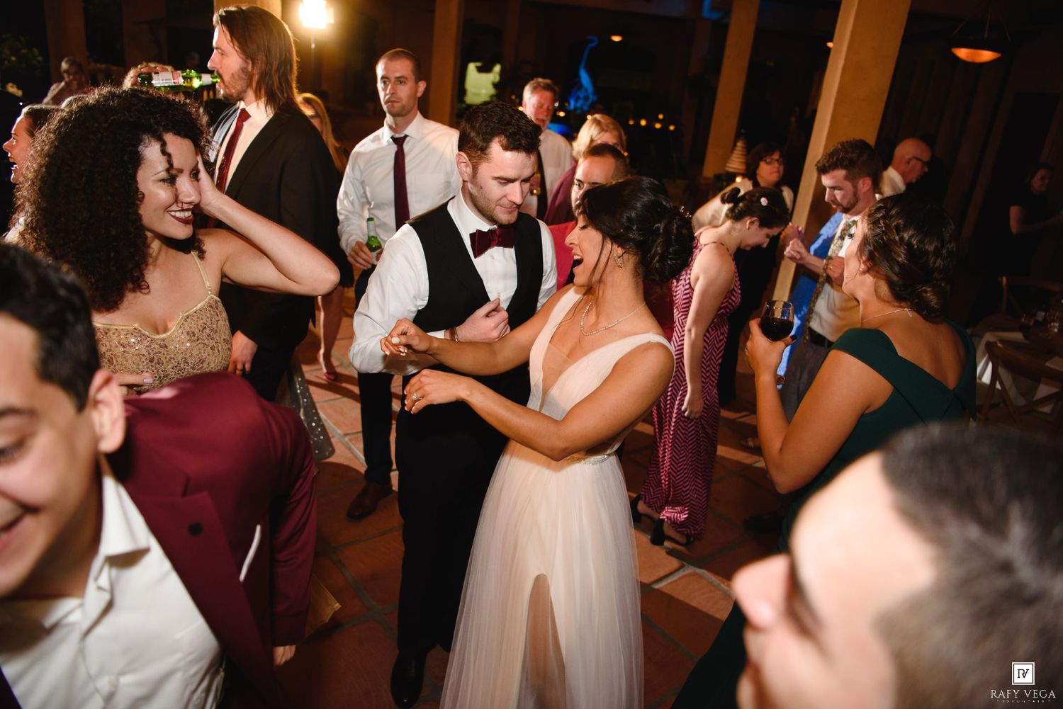 Bride and groom share a romantic first dance surrounded by guests at a lively wedding reception.