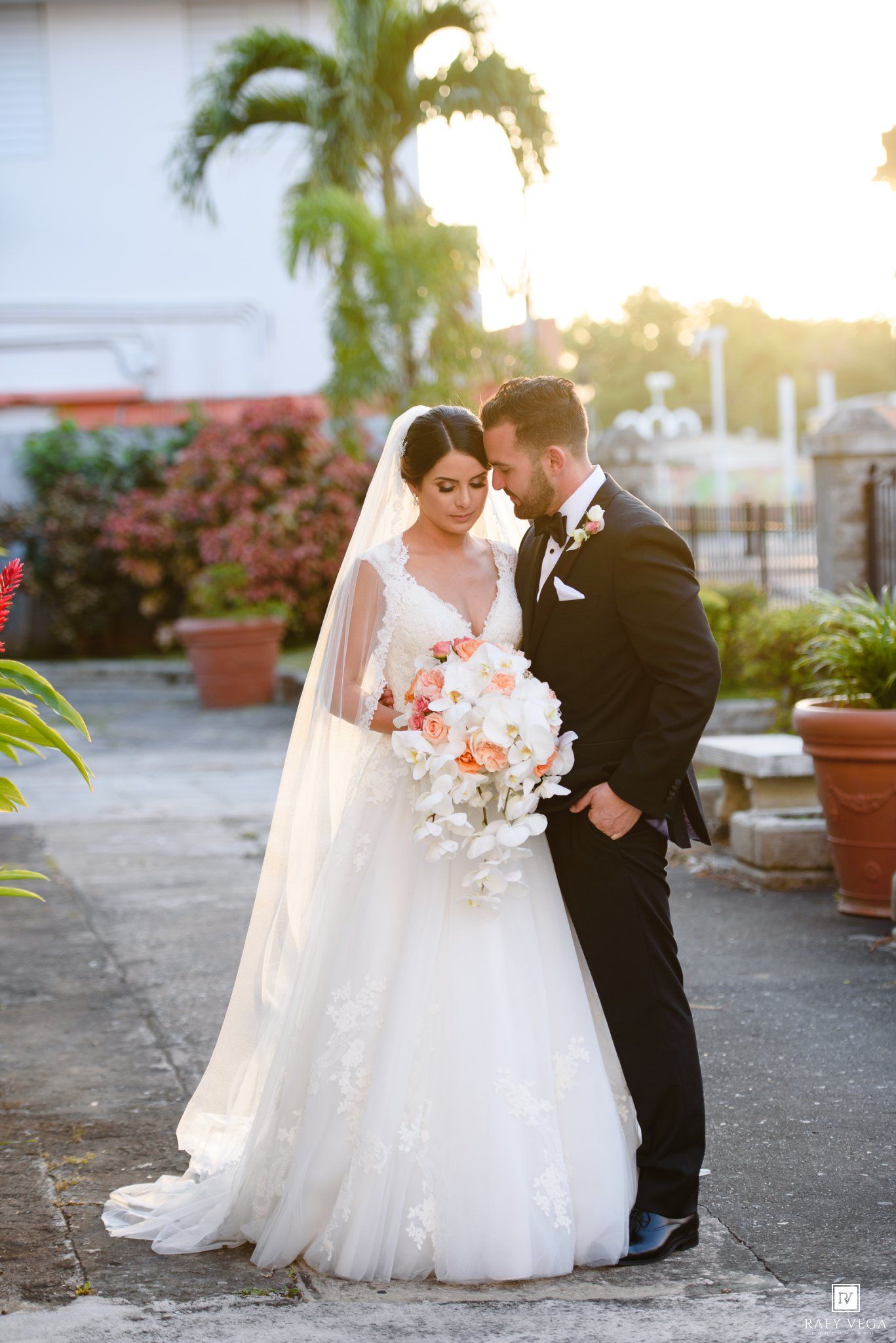 Bride and groom share an intimate moment outdoors at golden hour, bride holding a peach and white floral bouquet.