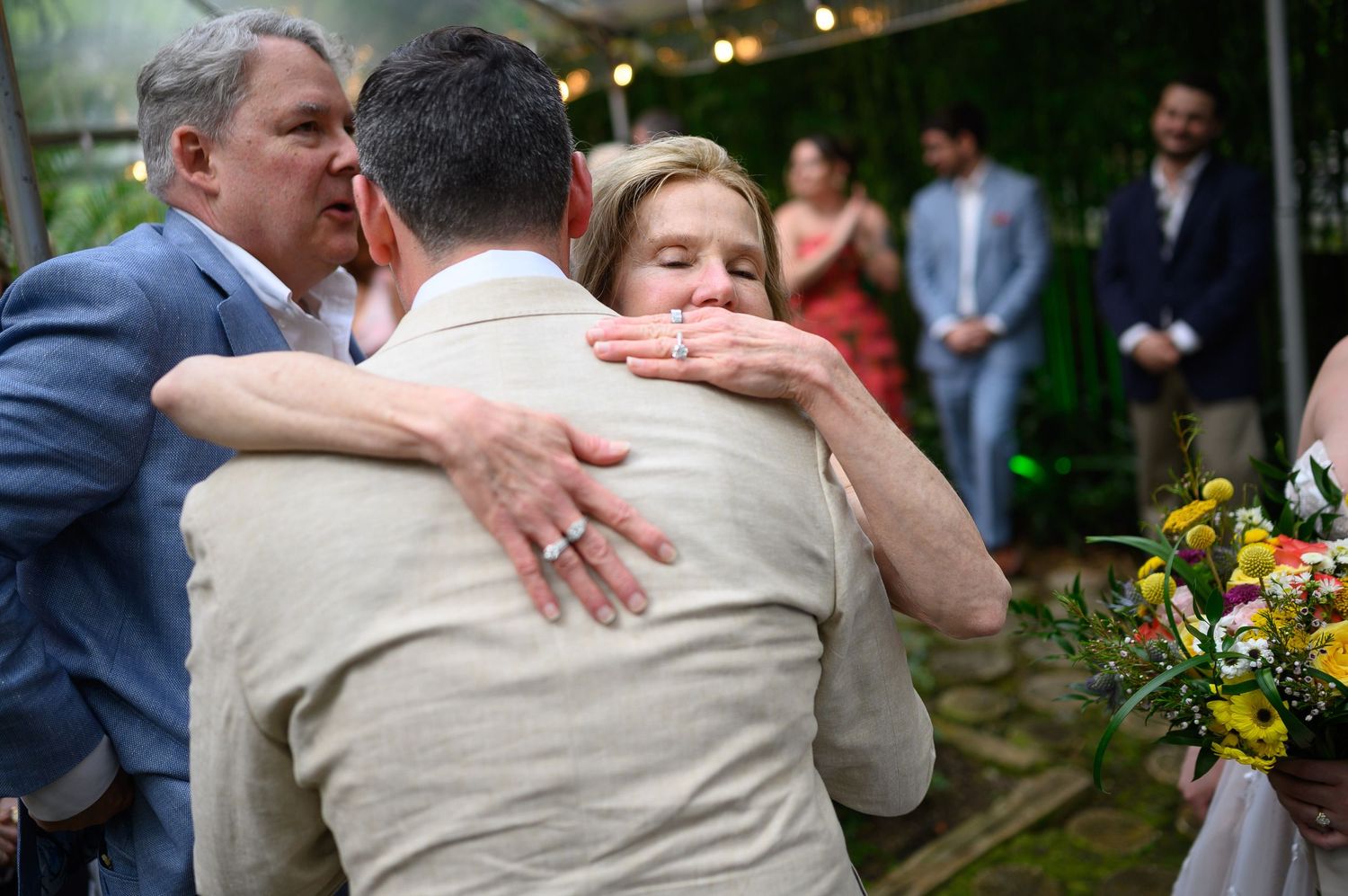 Emotional wedding moment as groom shares heartfelt group hug with family members during outdoor ceremony.