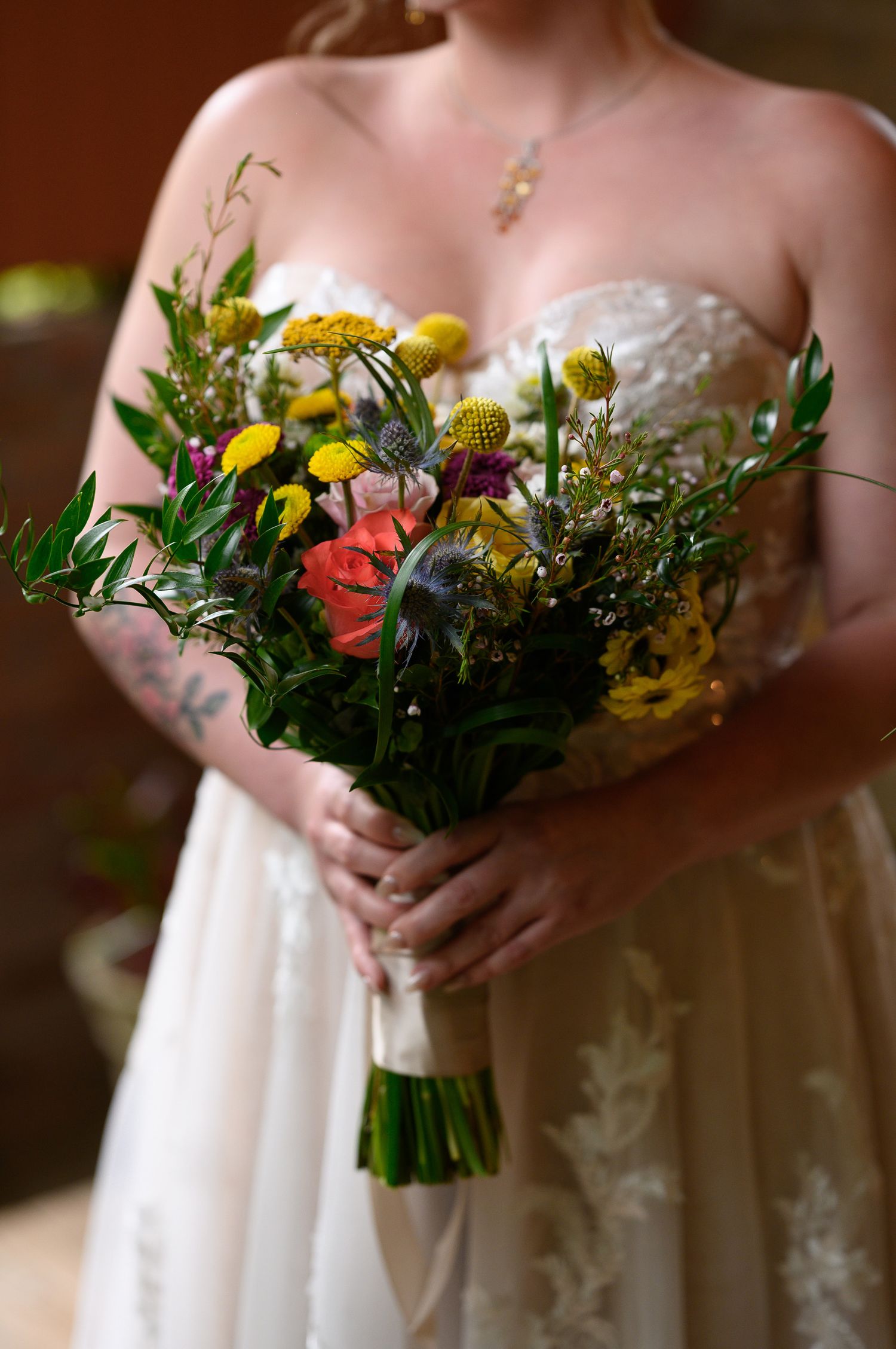 Bride in strapless lace gown holding vibrant wildflower bouquet with yellow, coral, and purple blooms.