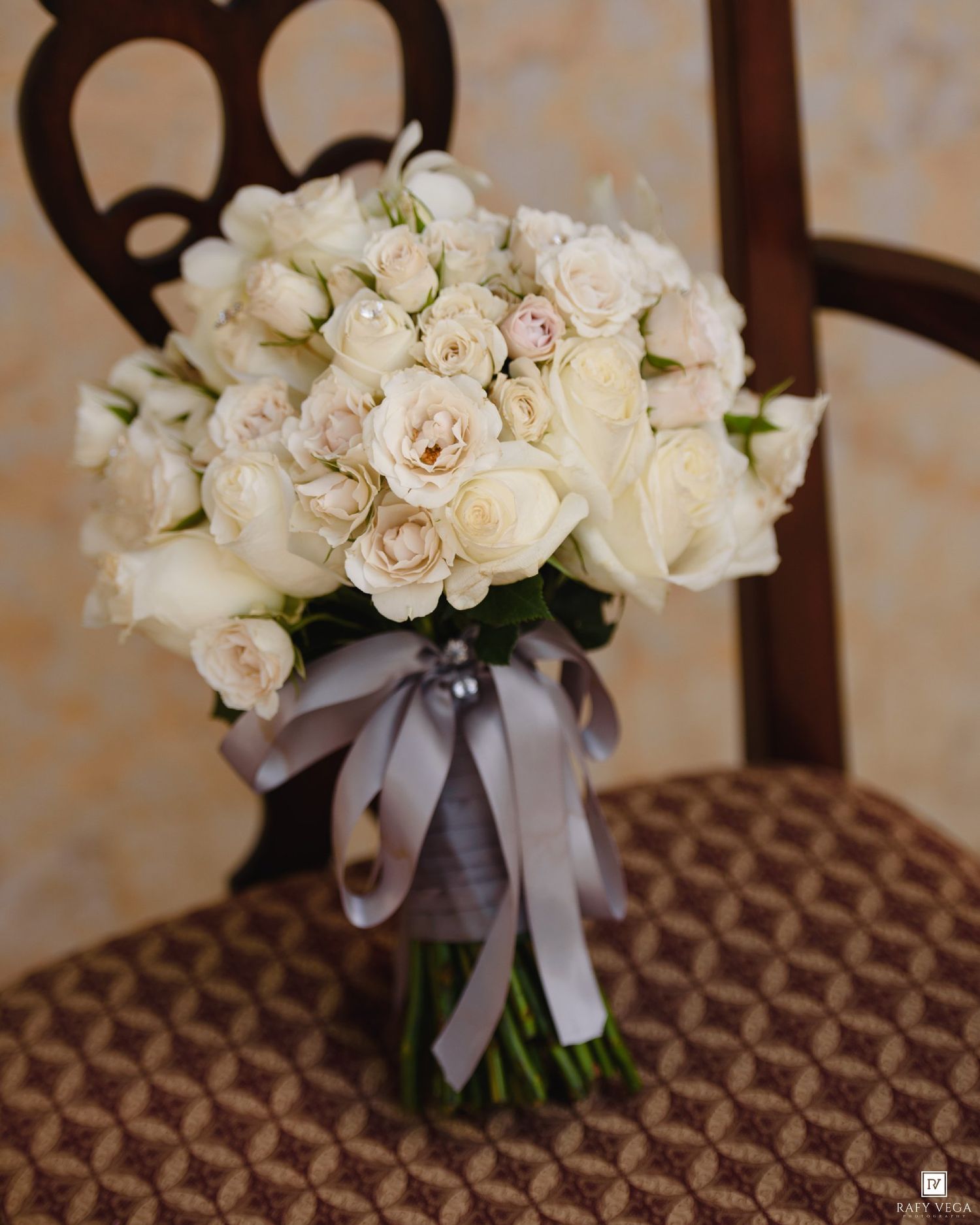 Elegant bridal bouquet of white and blush roses tied with gray ribbon, resting on a wooden chair.