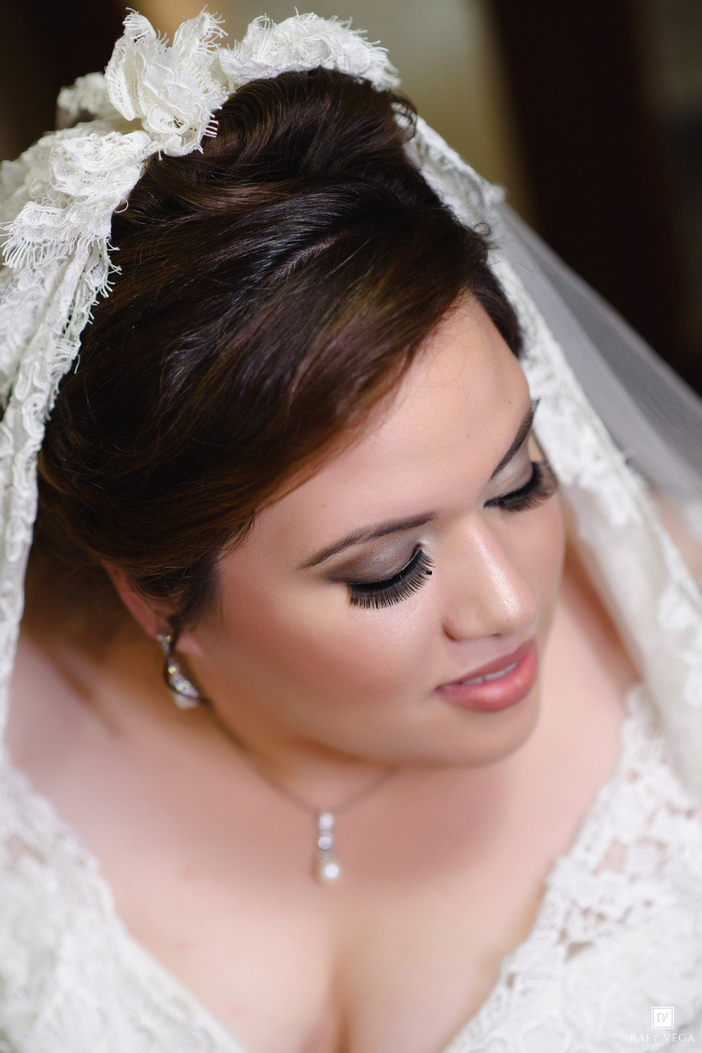 Close-up portrait of a beautiful bride wearing lace veil, pearl jewelry, and elegant makeup on her wedding day.