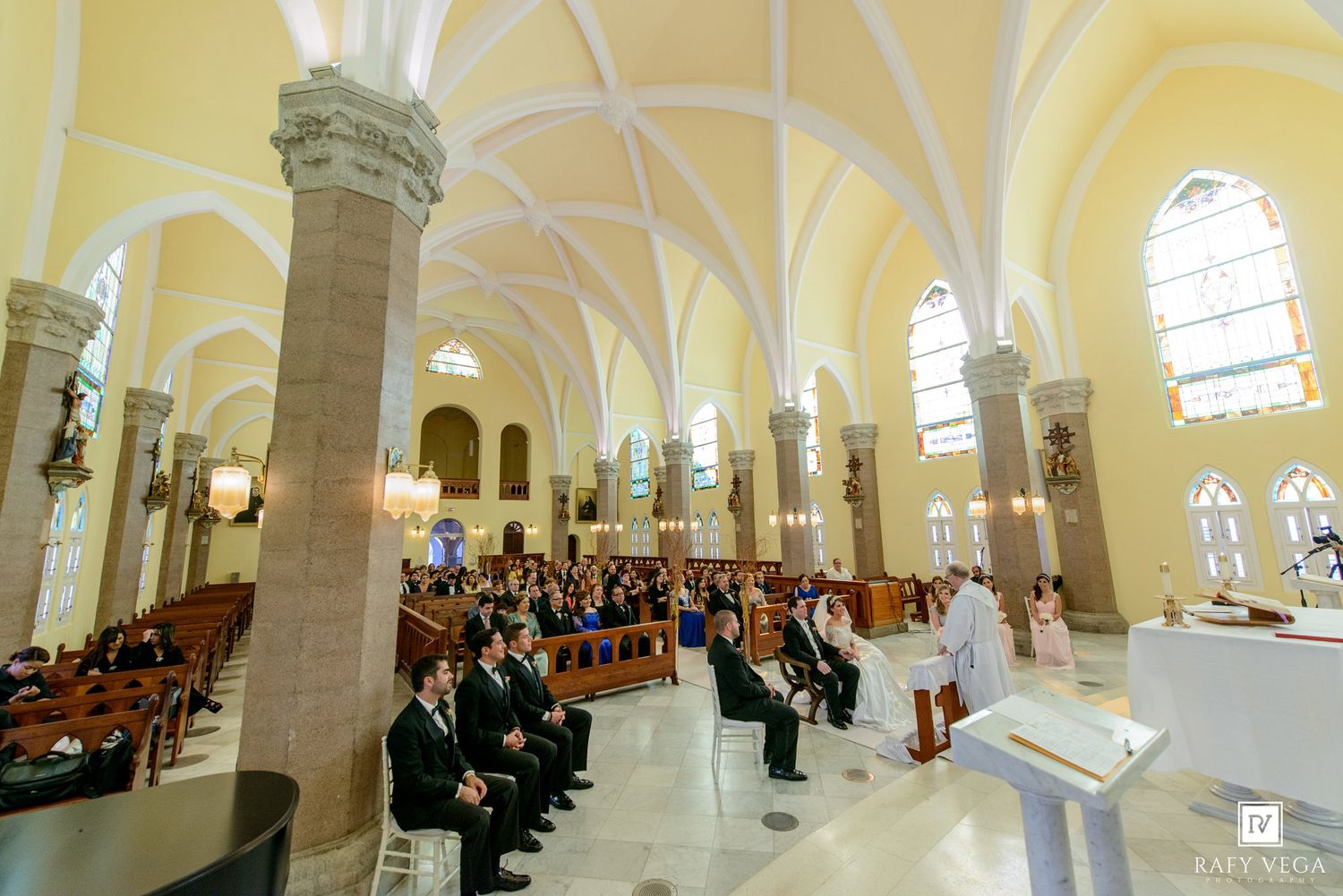 Elegant church wedding ceremony with guests seated in pews beneath Gothic arched ceilings and stained glass windows.