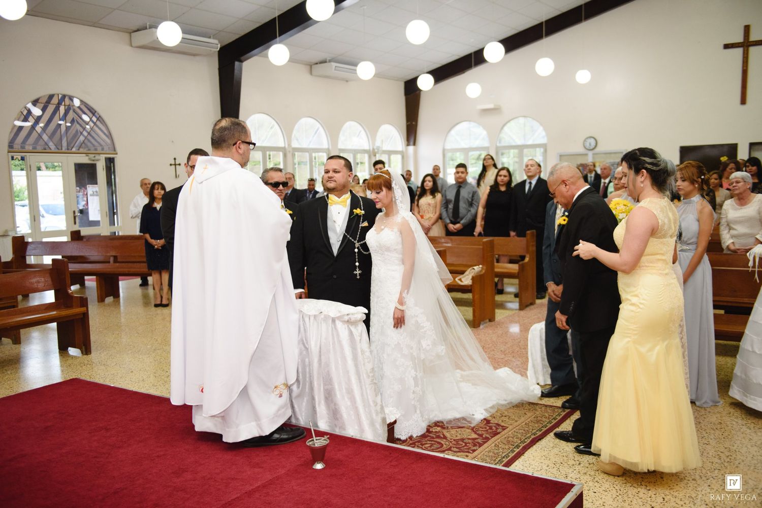 A bride and groom stand before a priest at the altar during a church wedding ceremony with guests looking on.