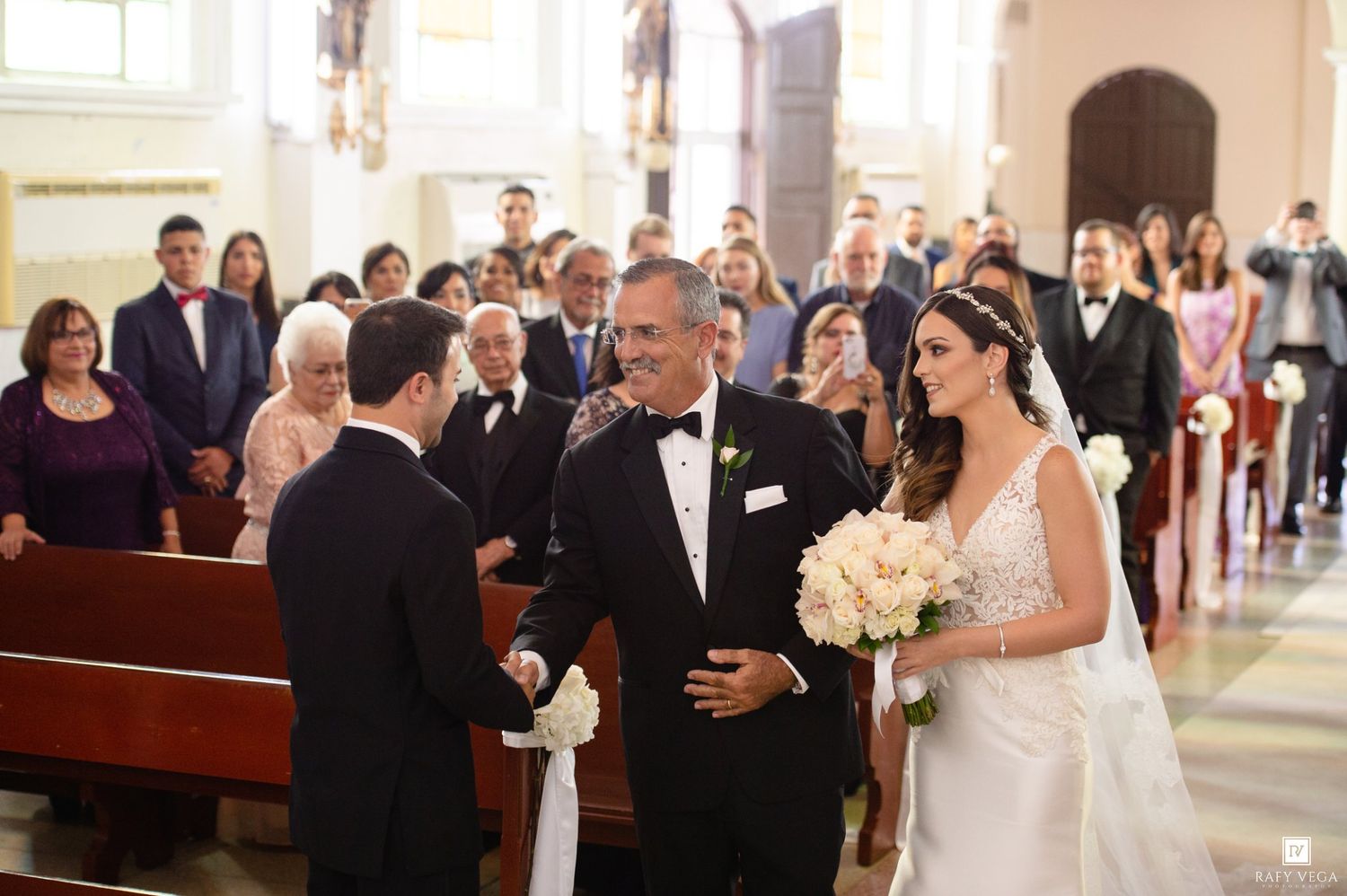 Bride in white gown walks down church aisle with father during elegant wedding ceremony.