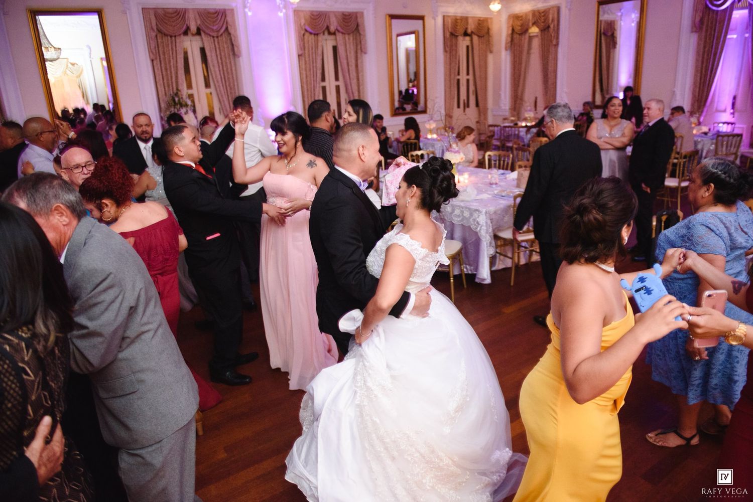 Bride and groom share first dance surrounded by guests in elegant ballroom wedding reception.