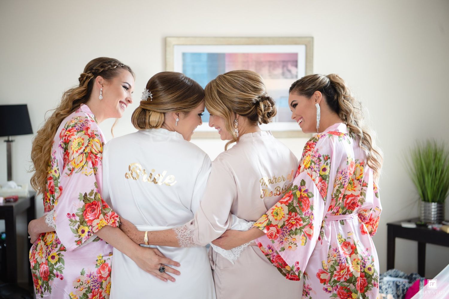 Bridesmaids in floral robes huddle together in a heartfelt moment during wedding preparations.