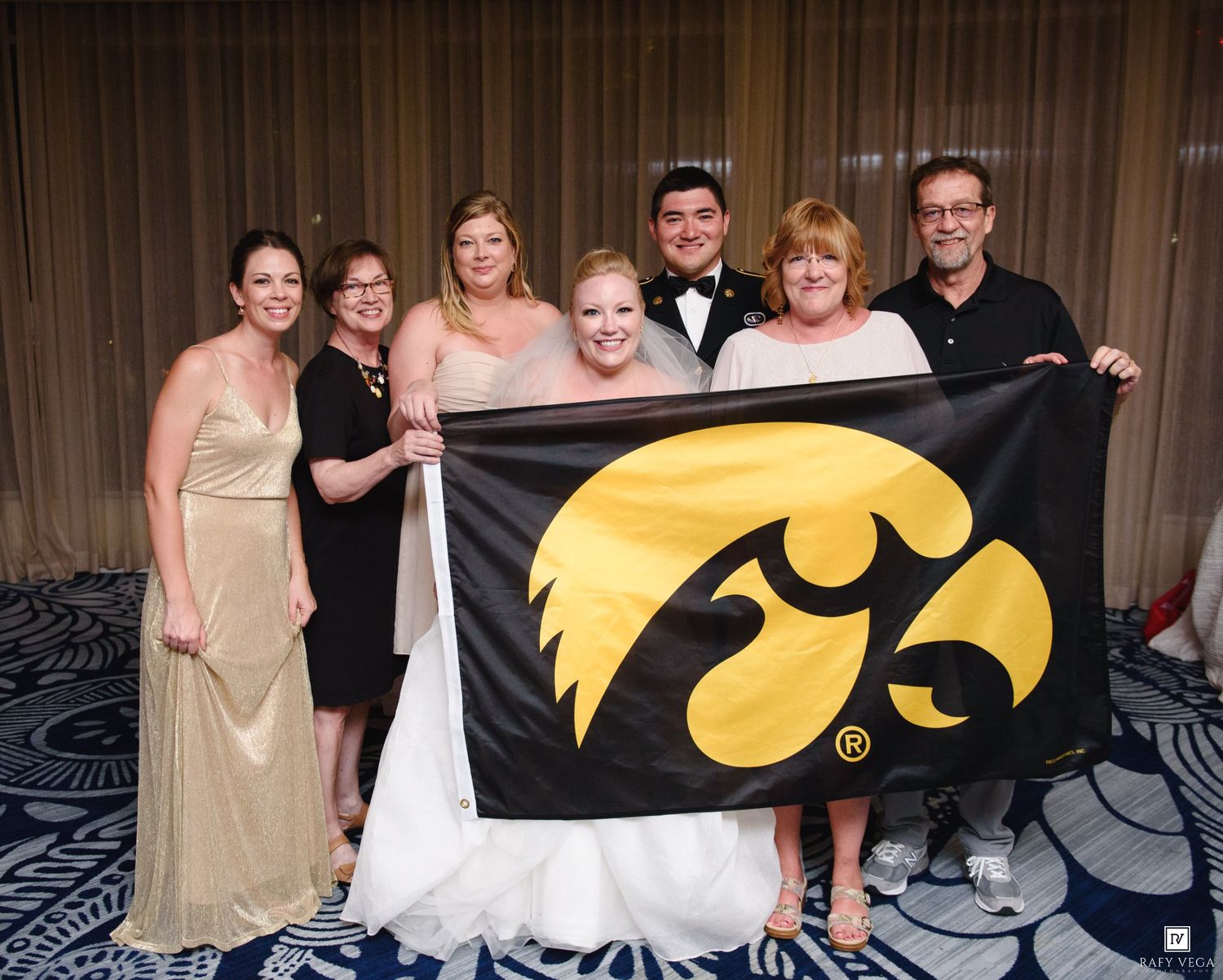Wedding party proudly holds Iowa Hawkeyes flag at elegant indoor reception celebration.