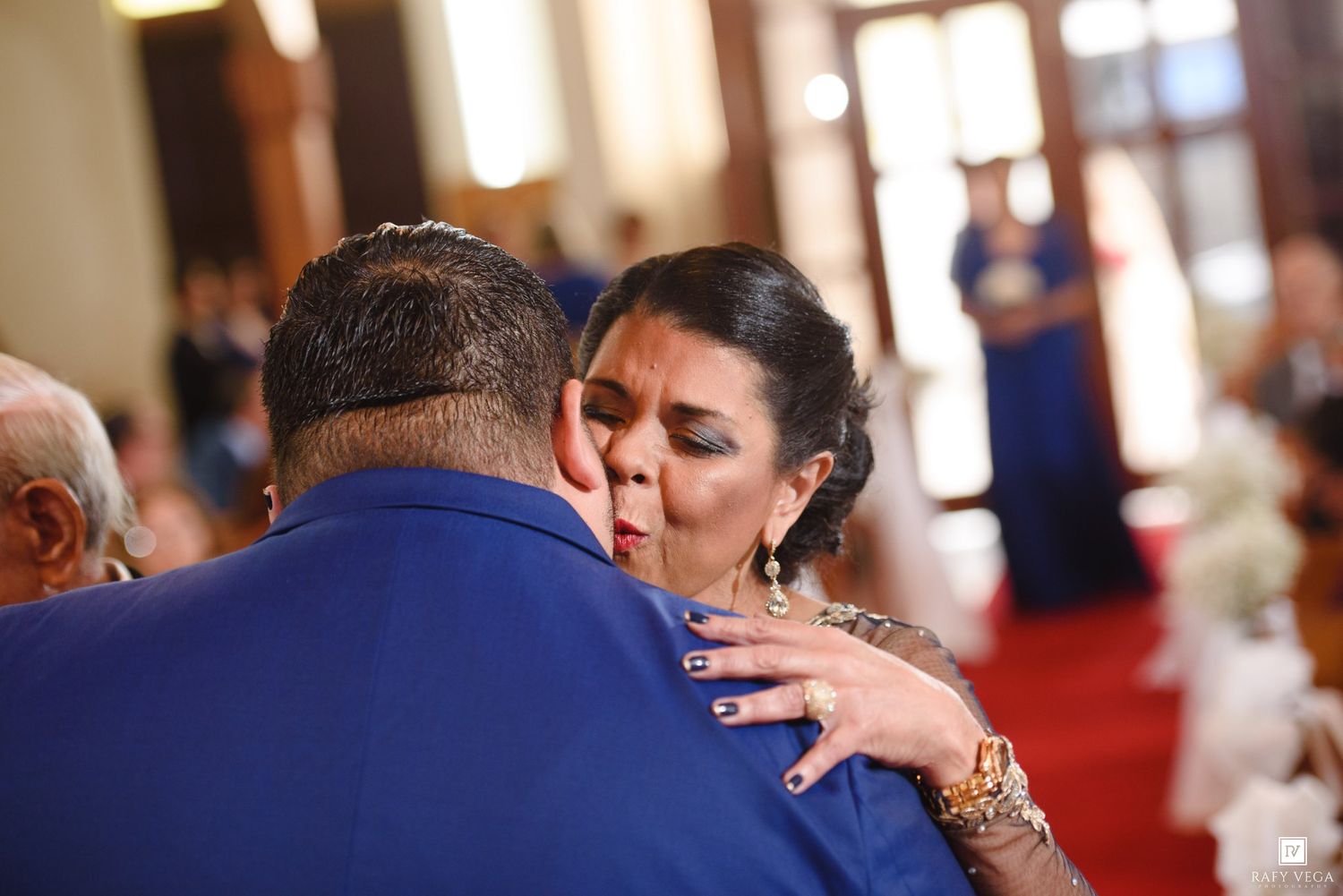 A woman in elegant attire embraces a man in a blue suit during an emotional wedding ceremony moment.