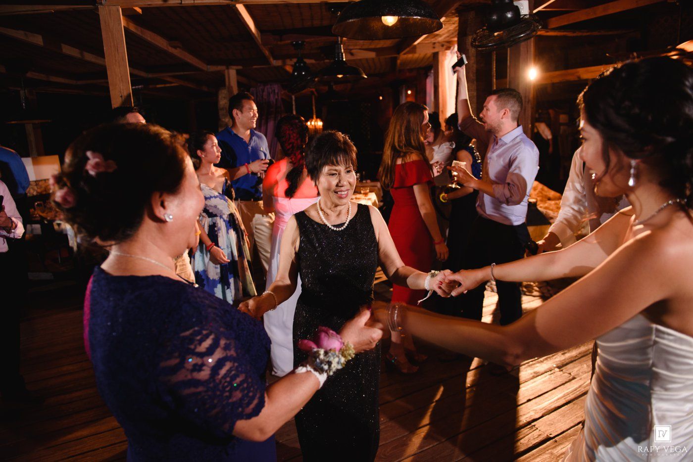 Wedding guests dance joyfully with the bride during lively indoor reception celebration.