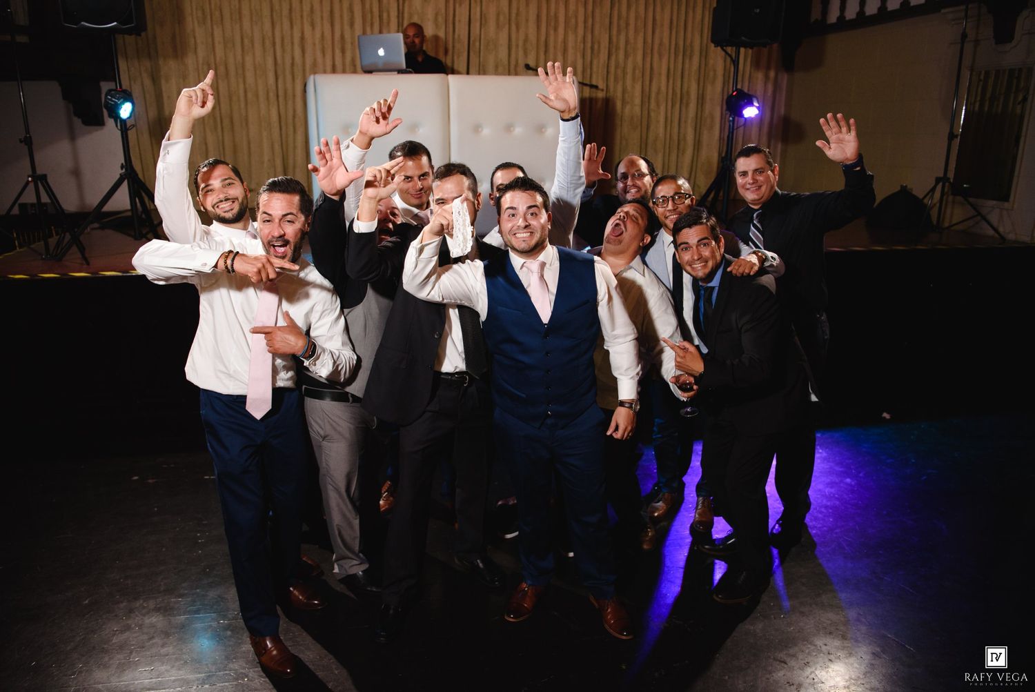 Groom and groomsmen celebrating joyfully on the dance floor with hands raised at a wedding reception.