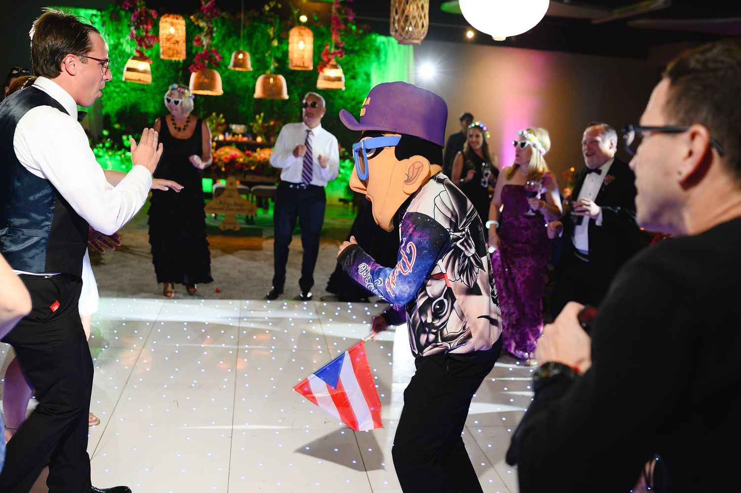 Guests dance with costumed character holding Puerto Rico flag at lively wedding reception celebration.