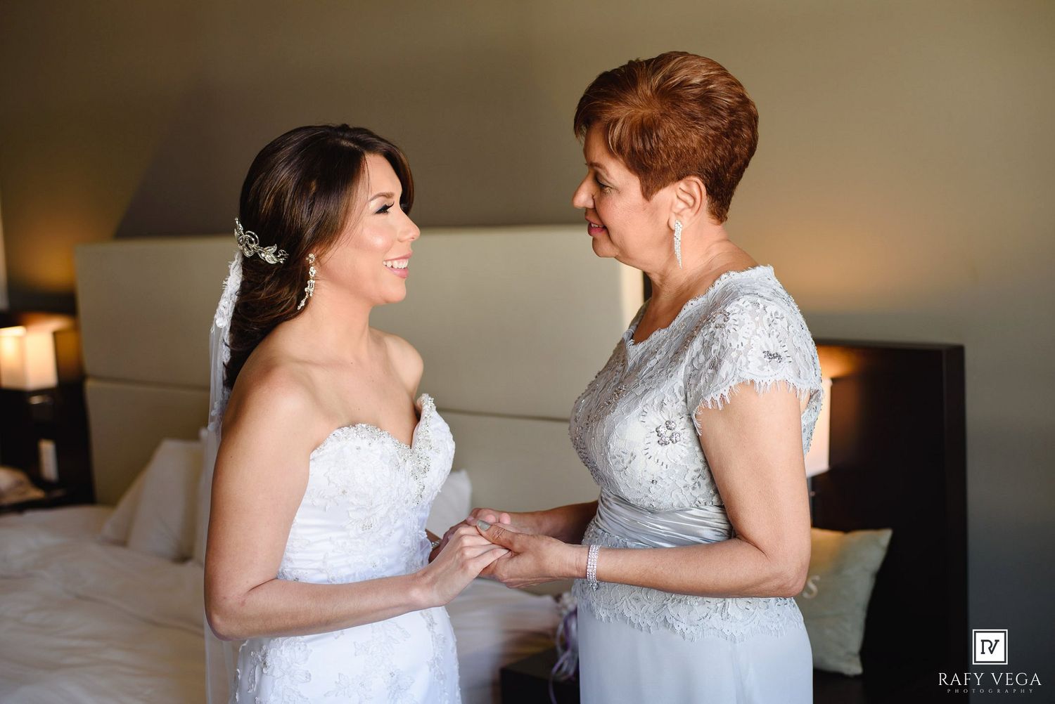 Bride and mother sharing a tender moment holding hands in a hotel room on wedding day.