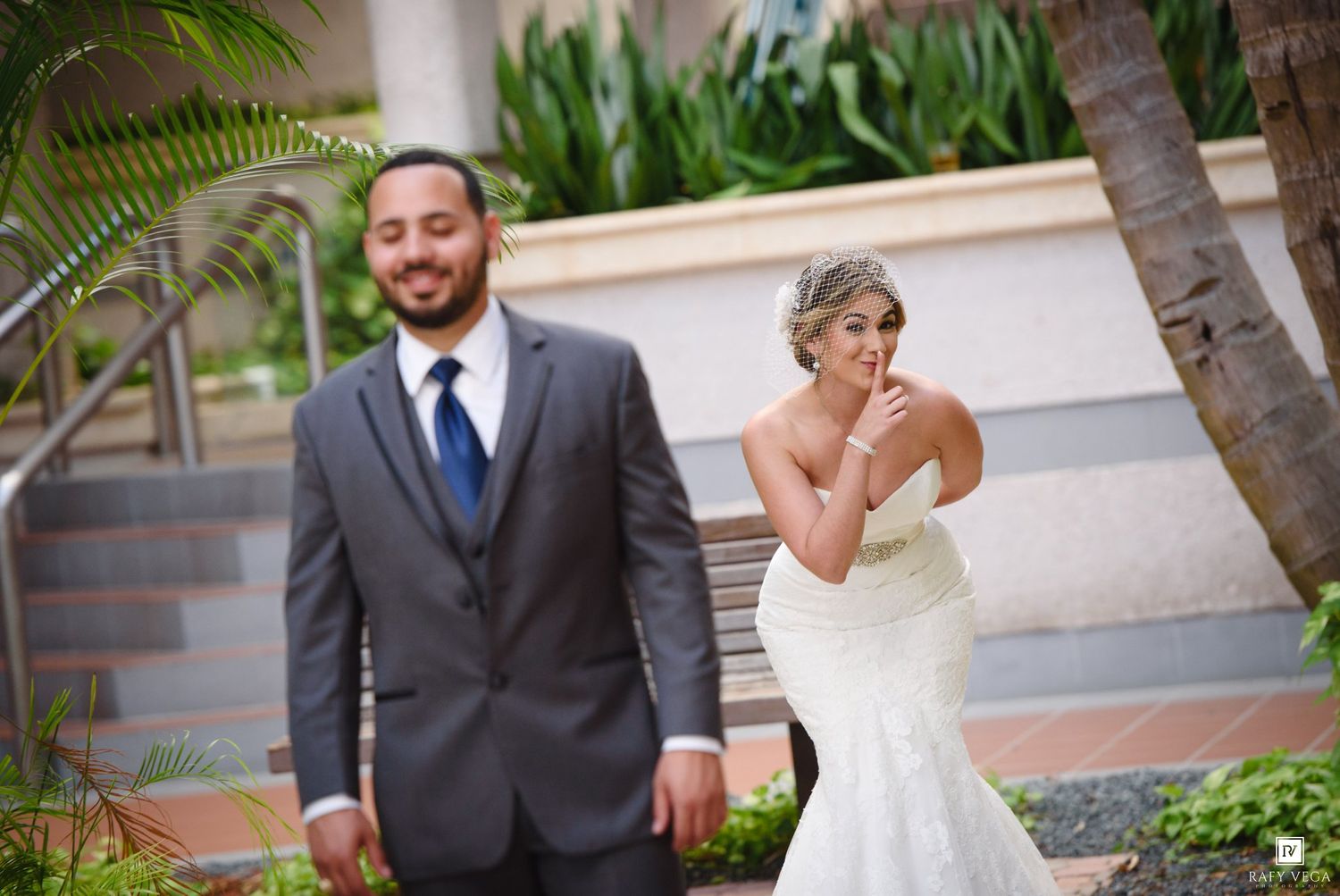 Bride in white mermaid gown covers her mouth in awe during first look with groom in gray suit outdoors.