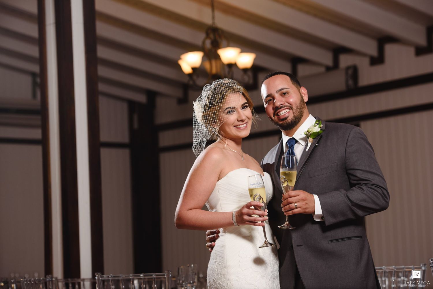 Bride and groom smiling and holding champagne glasses at their wedding reception in an elegant venue.