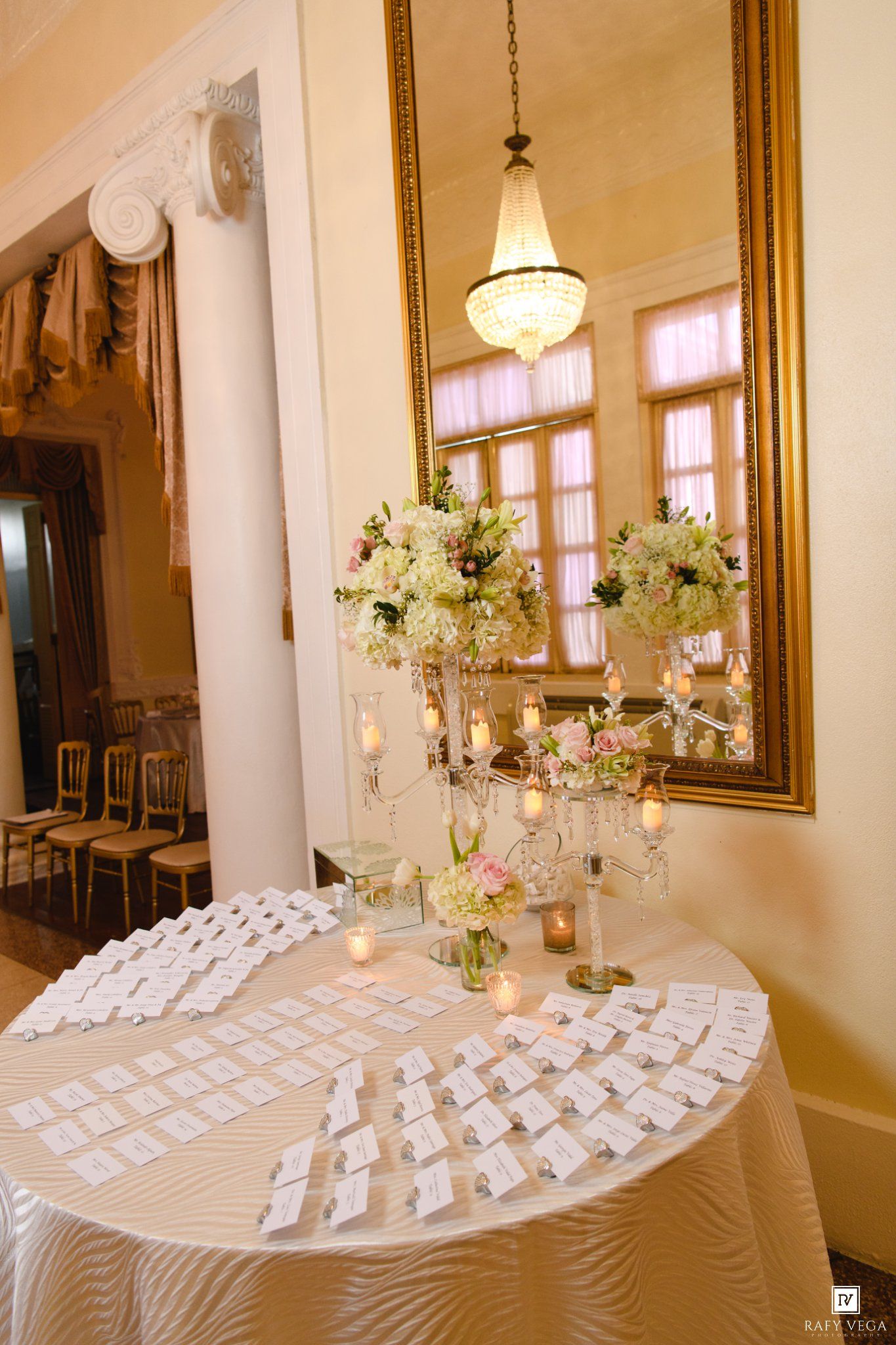 Elegant wedding reception escort card table with floral arrangements and gold mirror.